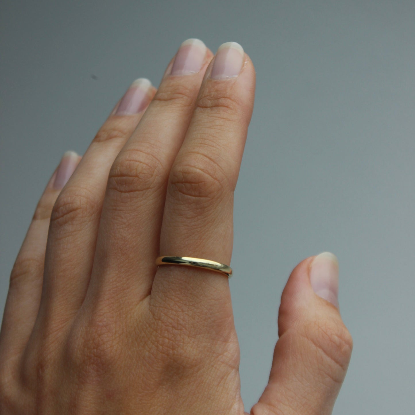 Hand wearing a gold ring on a plain background